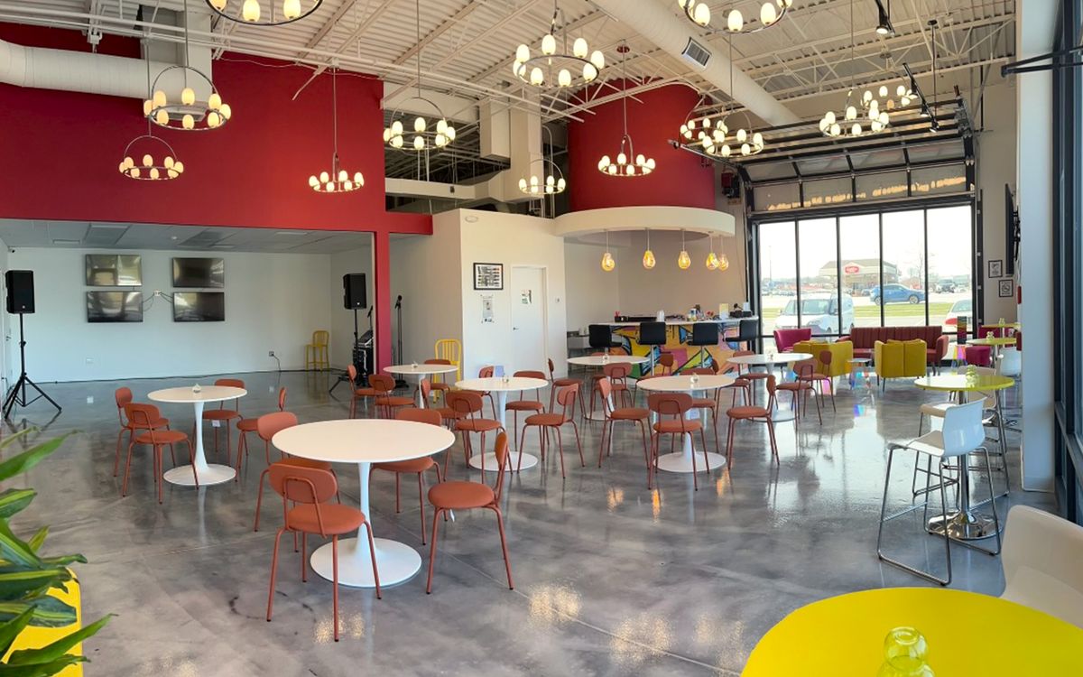 The members' lounge with round white tables, orange chairs and a red feature wall