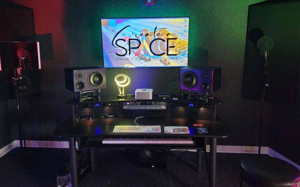 The music room desk with studio monitors, a keyboard and a lit Create A Space screen