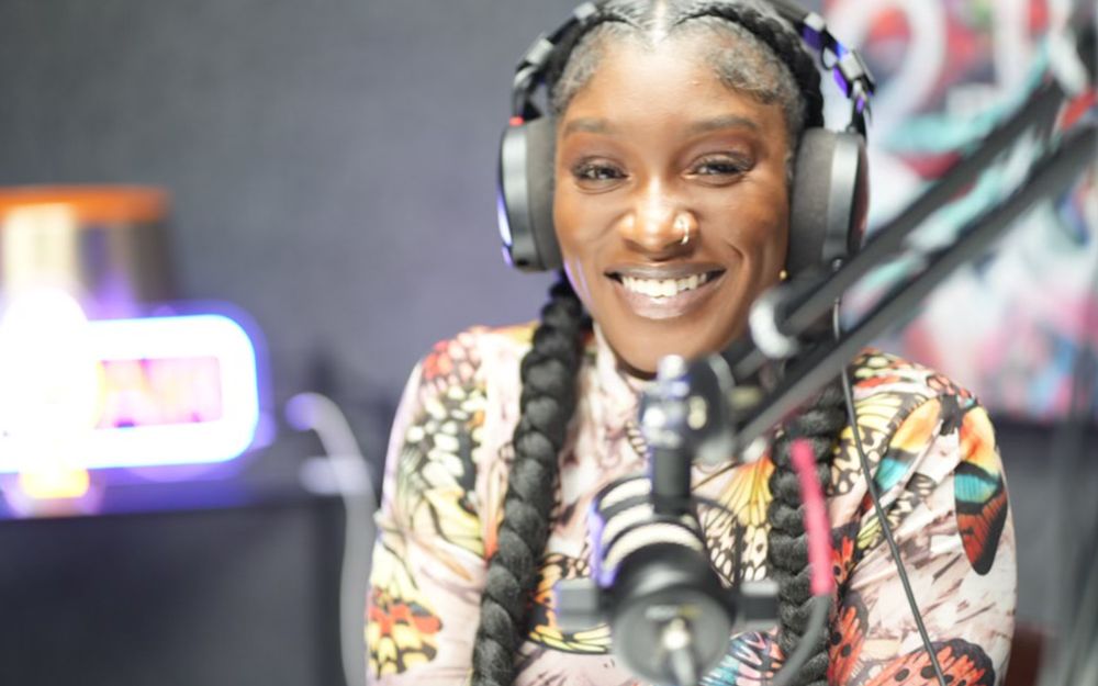 A smiling host wearing headphones in front of a studio microphone